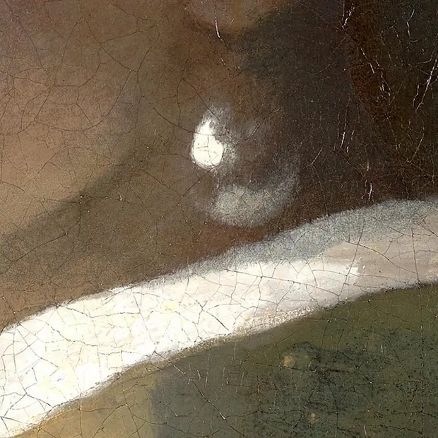 A close detail of the pearl earring showing that it is made of only two strokes, a bright highlight at the upper left and a soft grey reflected light along the lower edge, with the dark shadow of the neck between them and no painted outline.